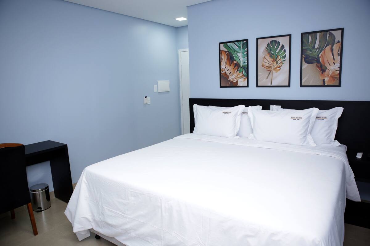 Une chambre d’hôtel avec un lit, un bureau et trois œuvres d’art représentant des feuilles tropicales, encadrées et accrochées au mur.