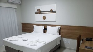 Ein ordentlich bezogenes Bett mit weißen Leinentüchern und zwei Kissen, ein Holz-Kopfteil, ein an der Wand befestigtes Kunstwerk und ein Holztisch mit einem Telefon.