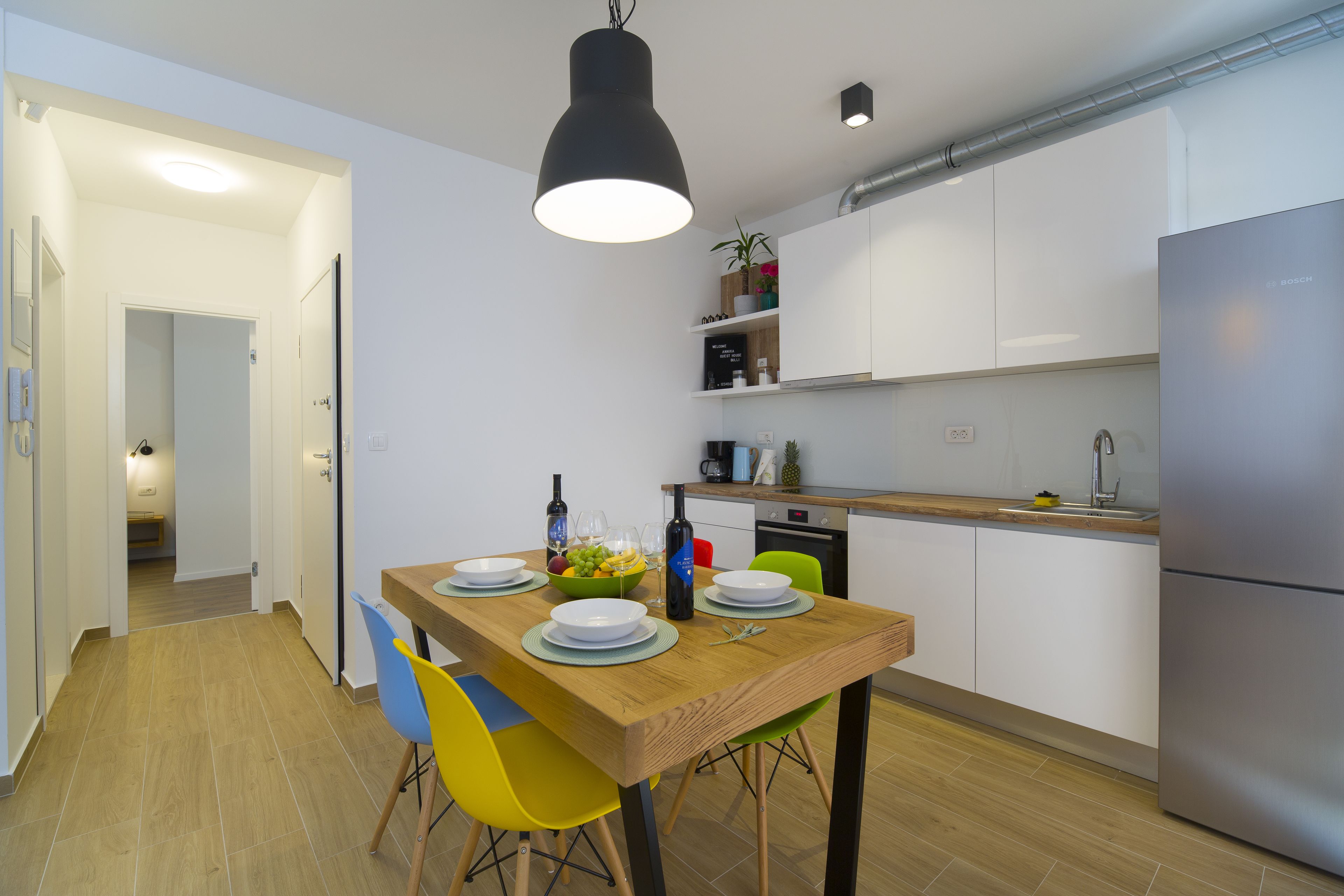 Una cocina moderna con armarios blancos, una mesa de comedor de madera y sillas coloridas.
