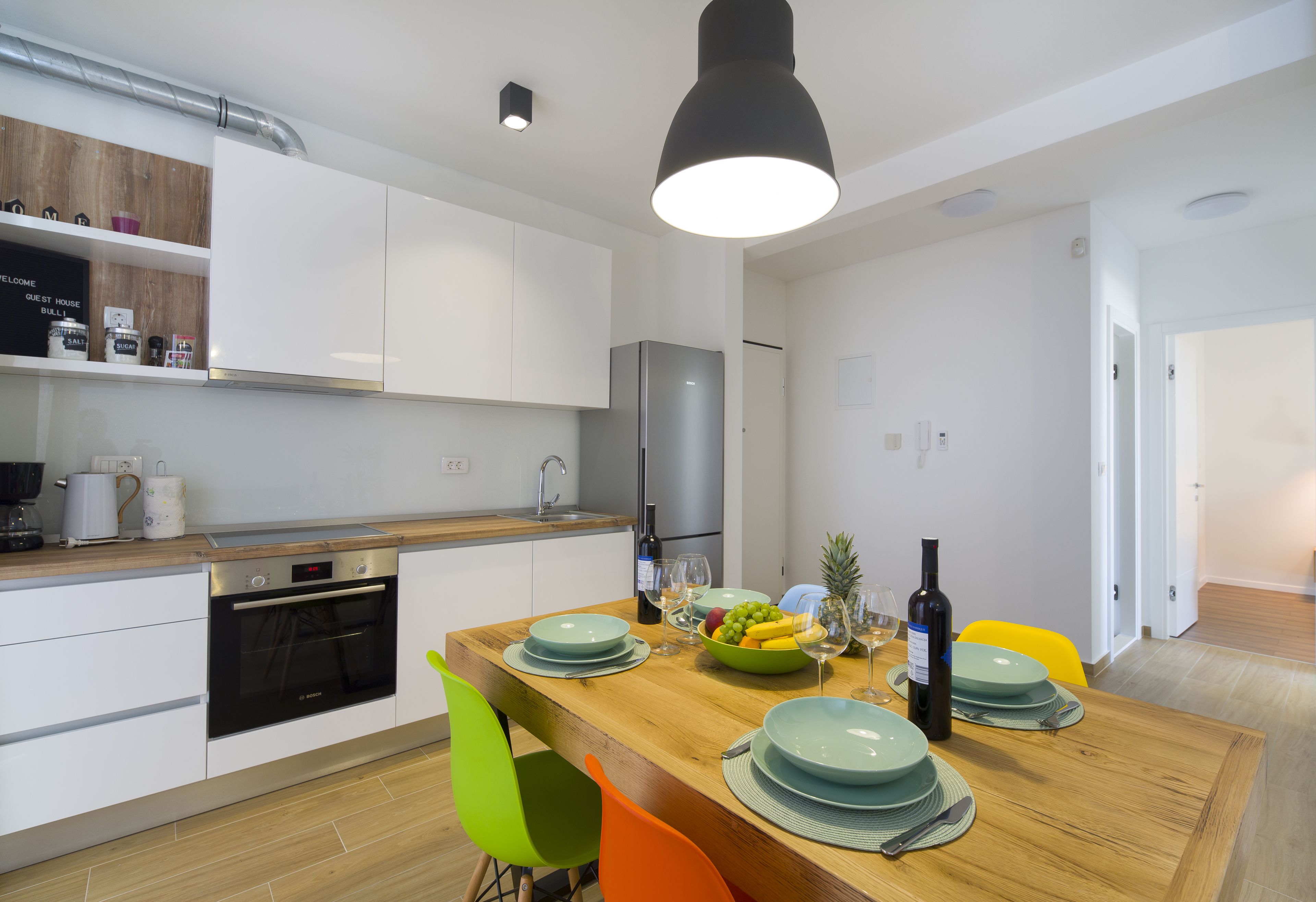 A modern kitchen with white cabinets, a wooden countertop, and a dining area with a wooden table set for four.