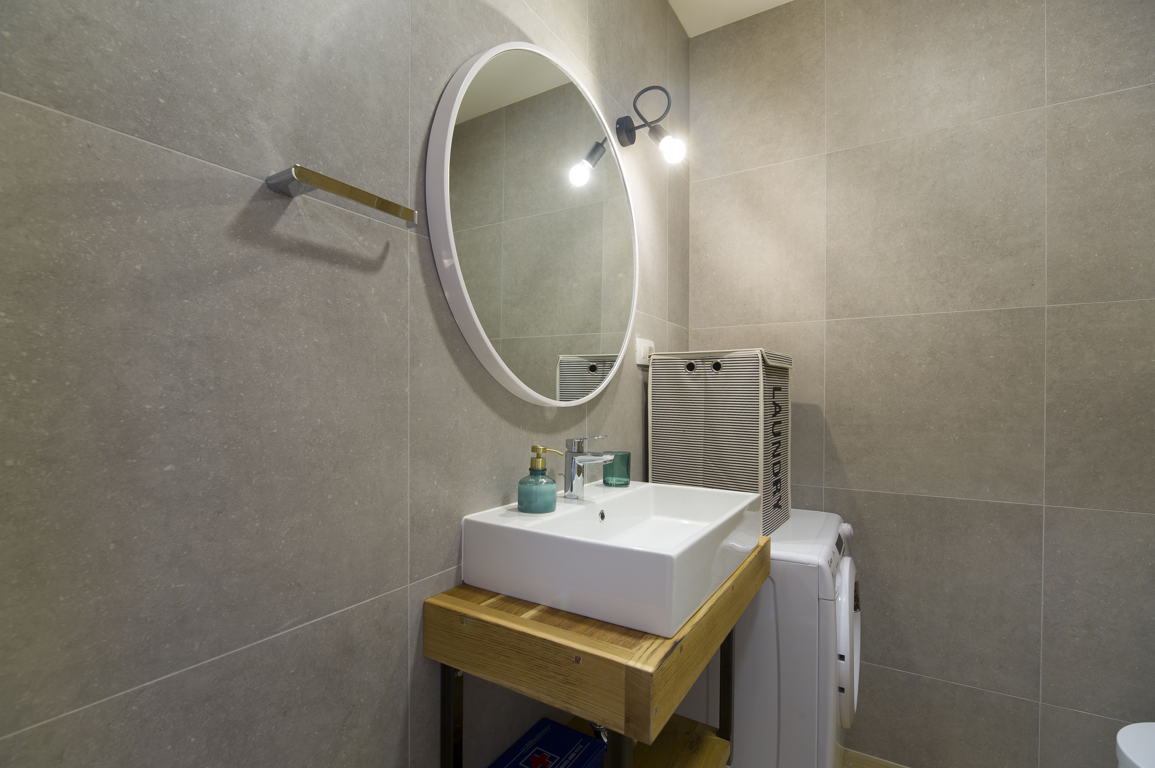 Un baño con un lavamanos blanco, un espejo y un perchero para toallas.