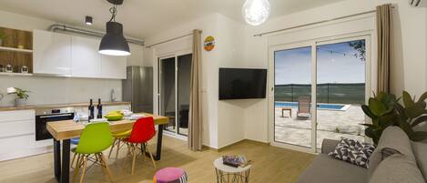 Una sala moderna con un sofá, una mesa de comedor con sillas coloridas, una pequeña mesa redonda con un libro y un ventanal con vistas a la playa.