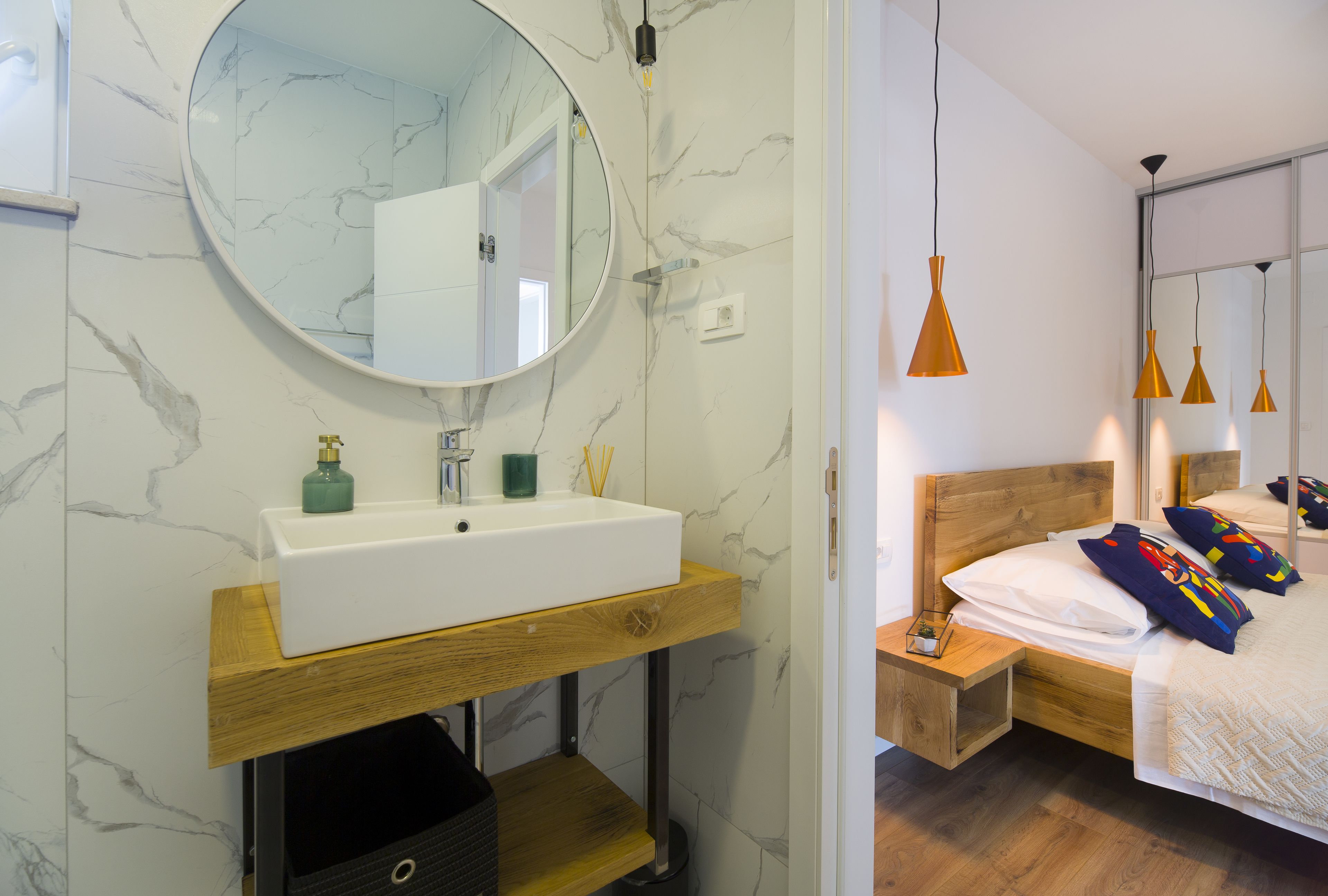 Ein modernes Badezimmer mit Marmorwand, einem runden Spiegel, einem weißen Waschbecken und einer Holzkommode.