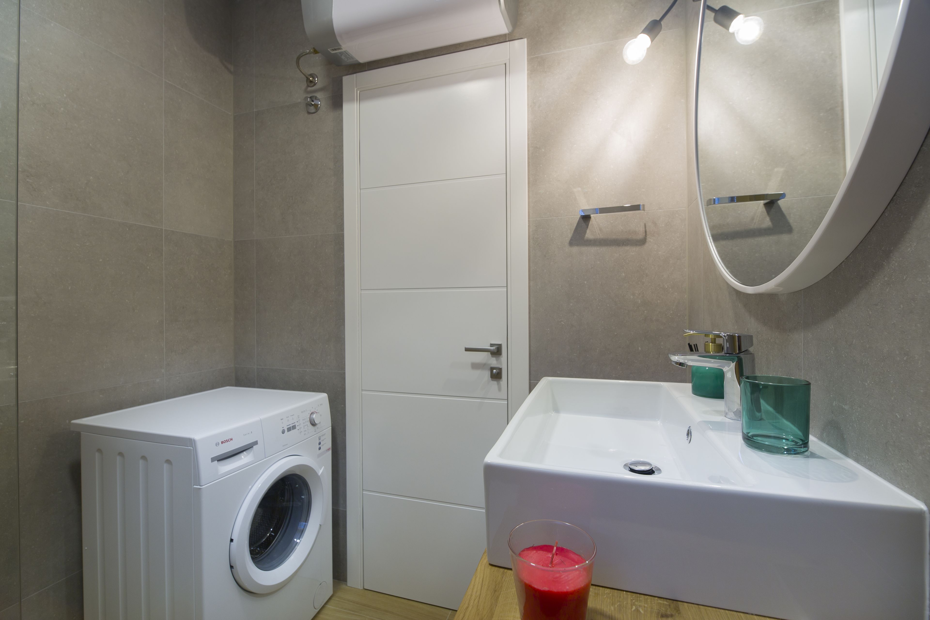 Ein modernes Badezimmer mit einer Waschmaschine, einem Waschbecken mit Spiegel und einem Glas rote Flüssigkeit auf der Ablagefläche.