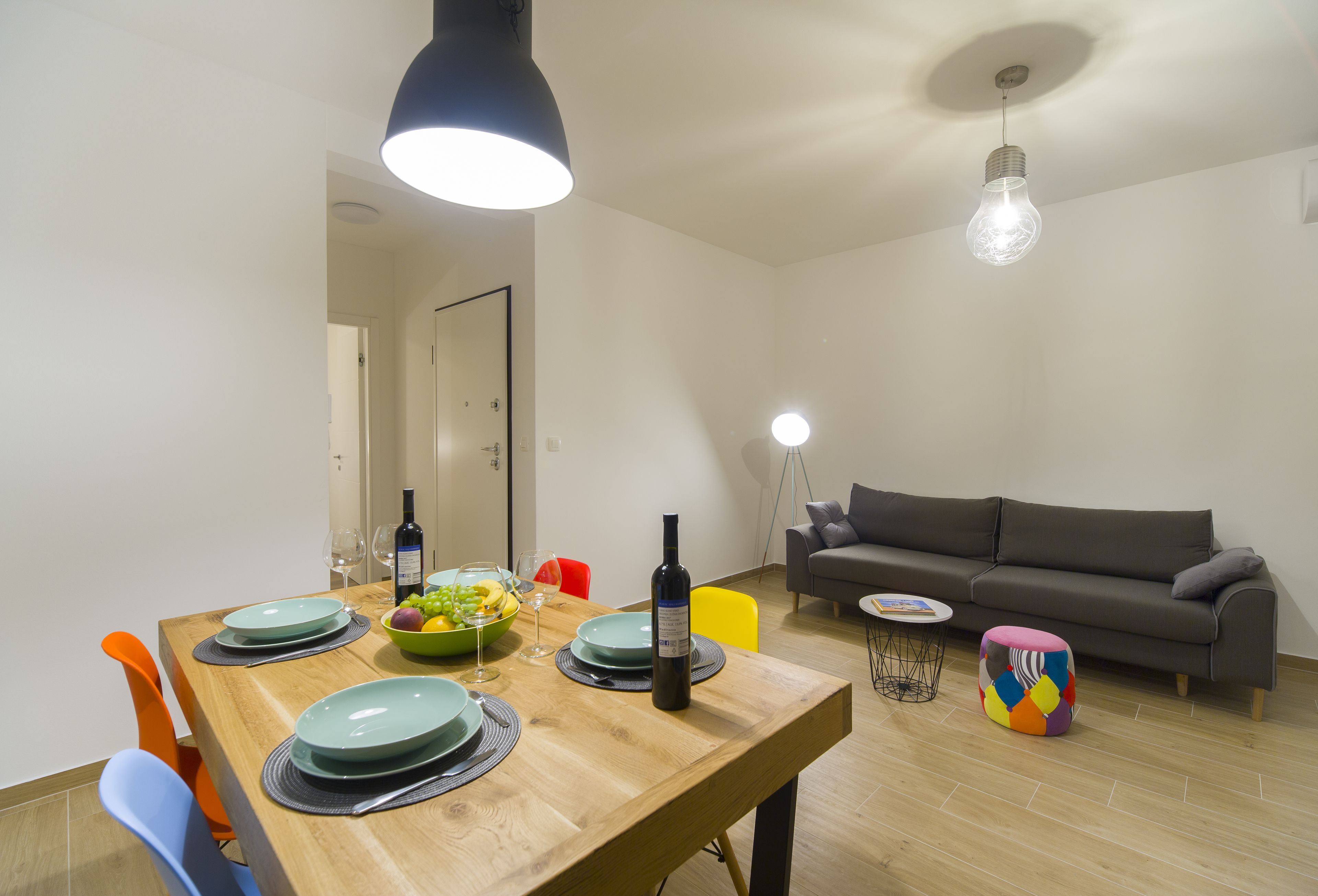 Un comedor con una mesa de madera dispuesta para cuatro personas, un sofá y un otomano colorido.