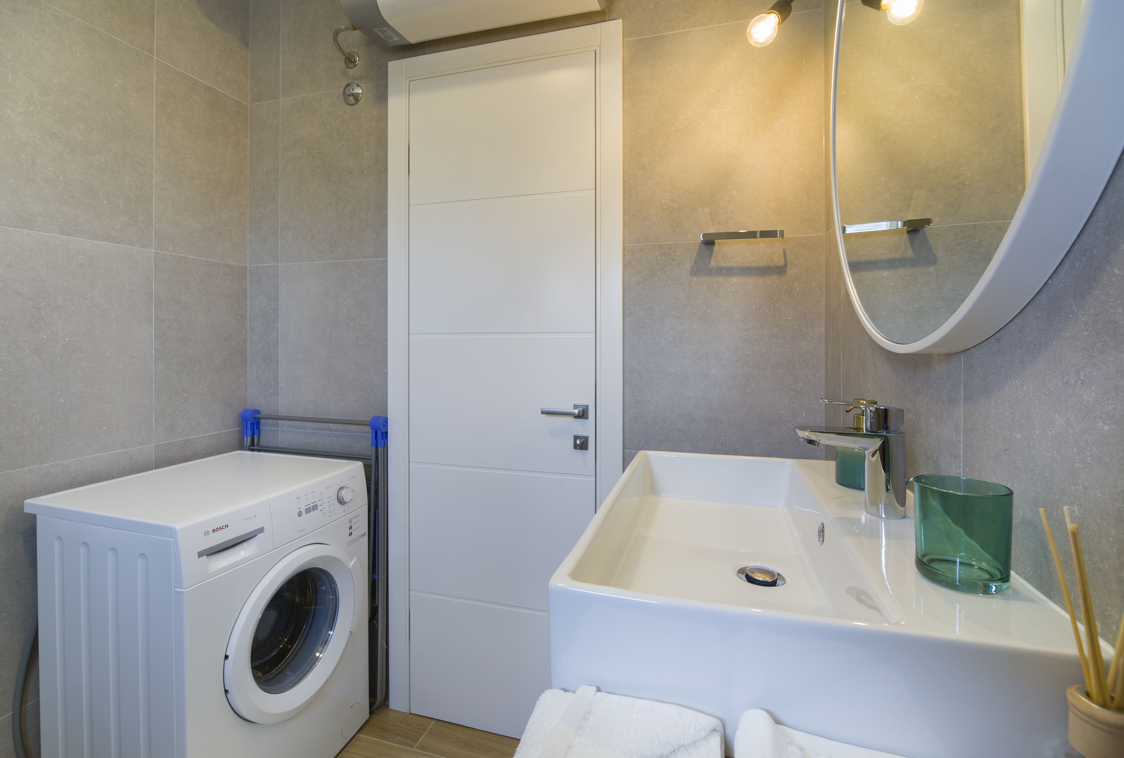 A compact bathroom with a washing machine, a sink with a mirror, and a towel rack.