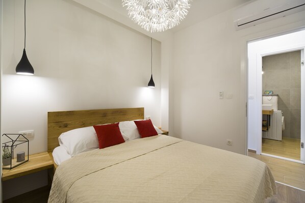 A bedroom with a wooden headboard, a bed with white and red pillows, two pendant lights, and a modern chandelier.