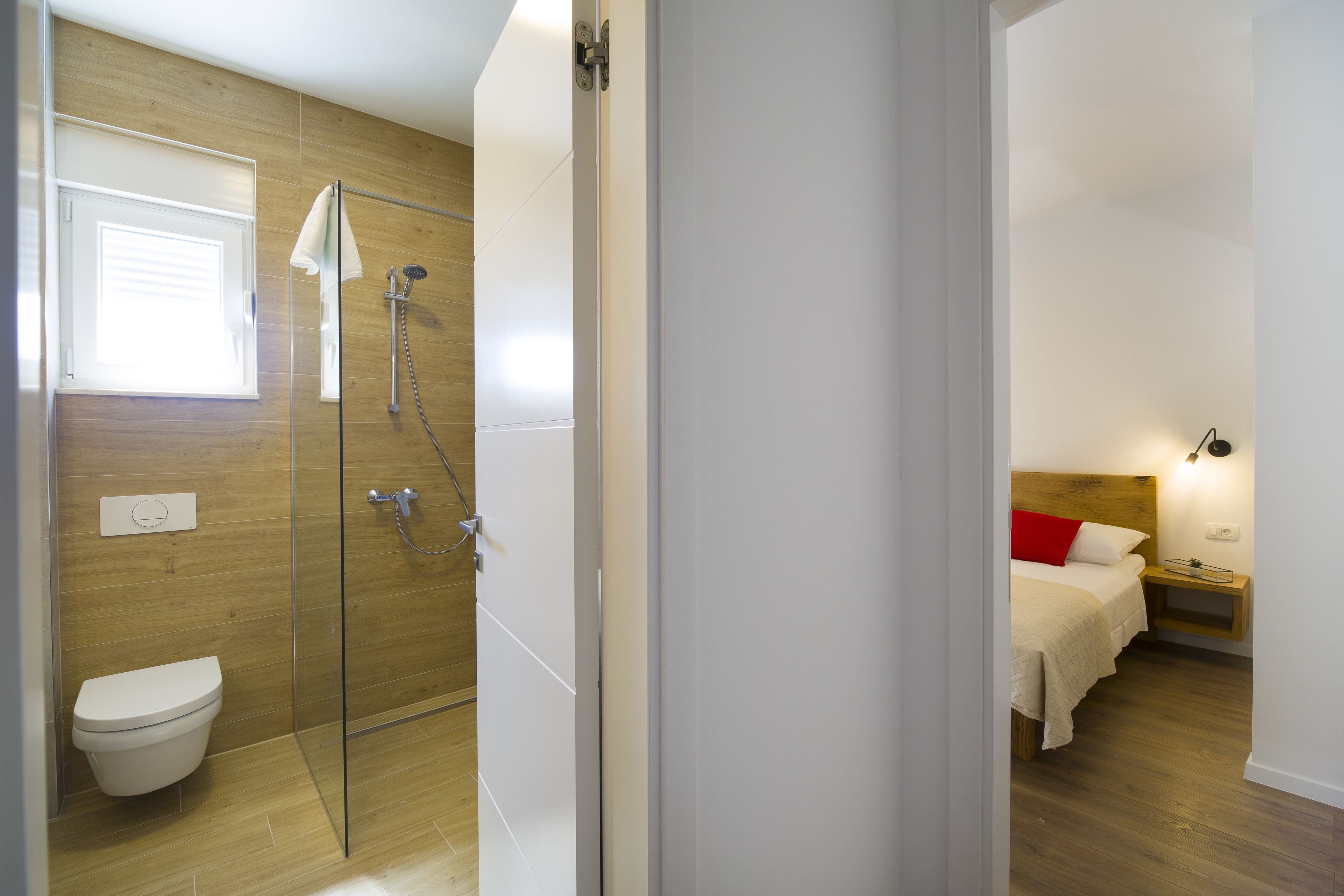 A modern bathroom with a glass shower enclosure, a toilet, and a wooden floor.