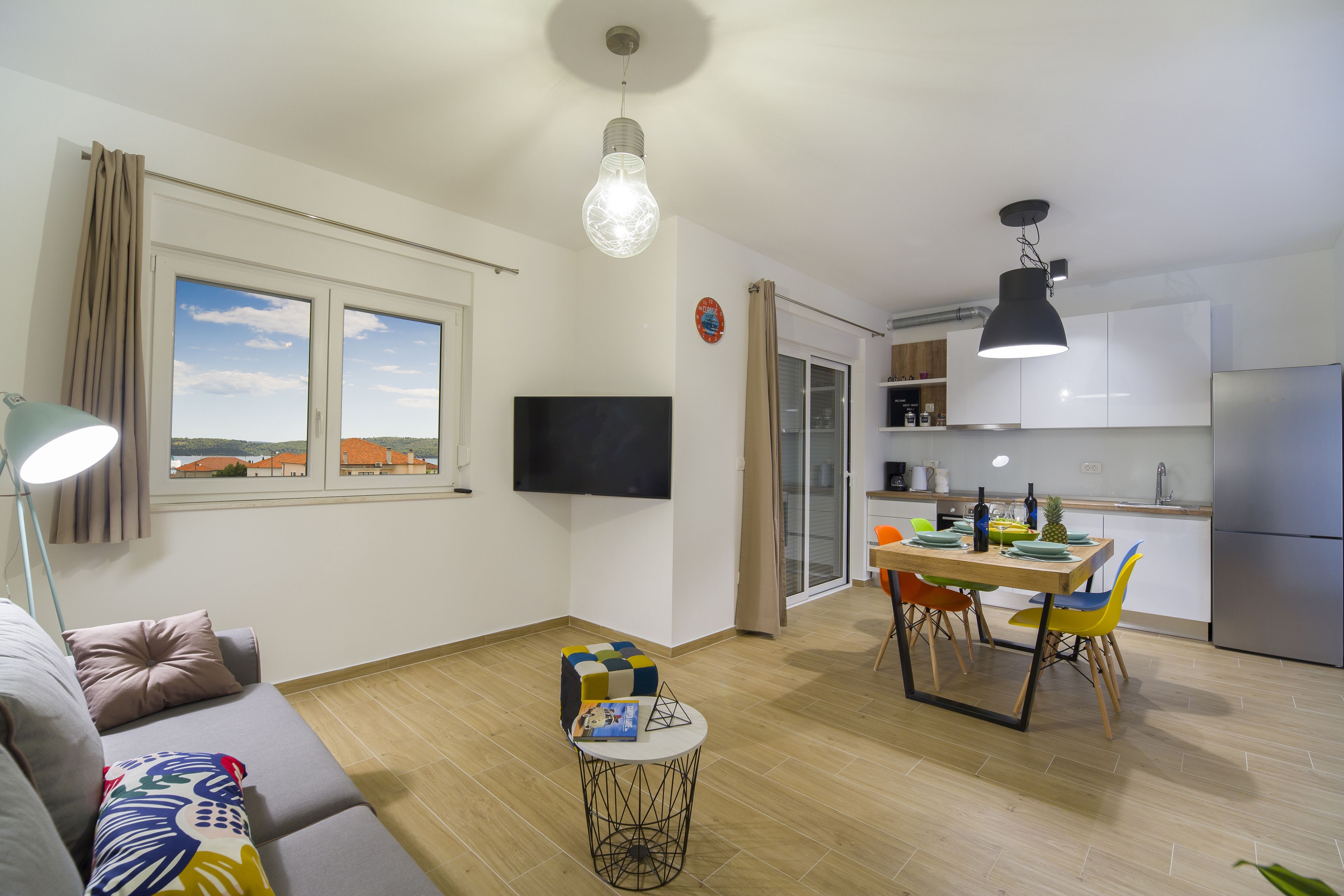 Un appartement moderne comprenant un espace de vie, un coin repas et une cuisine. Il est équipé d’un téléviseur à écran plat, d’une table à manger avec des chaises, ainsi que d’une cuisine avec des placards et des appareils électroménagers.