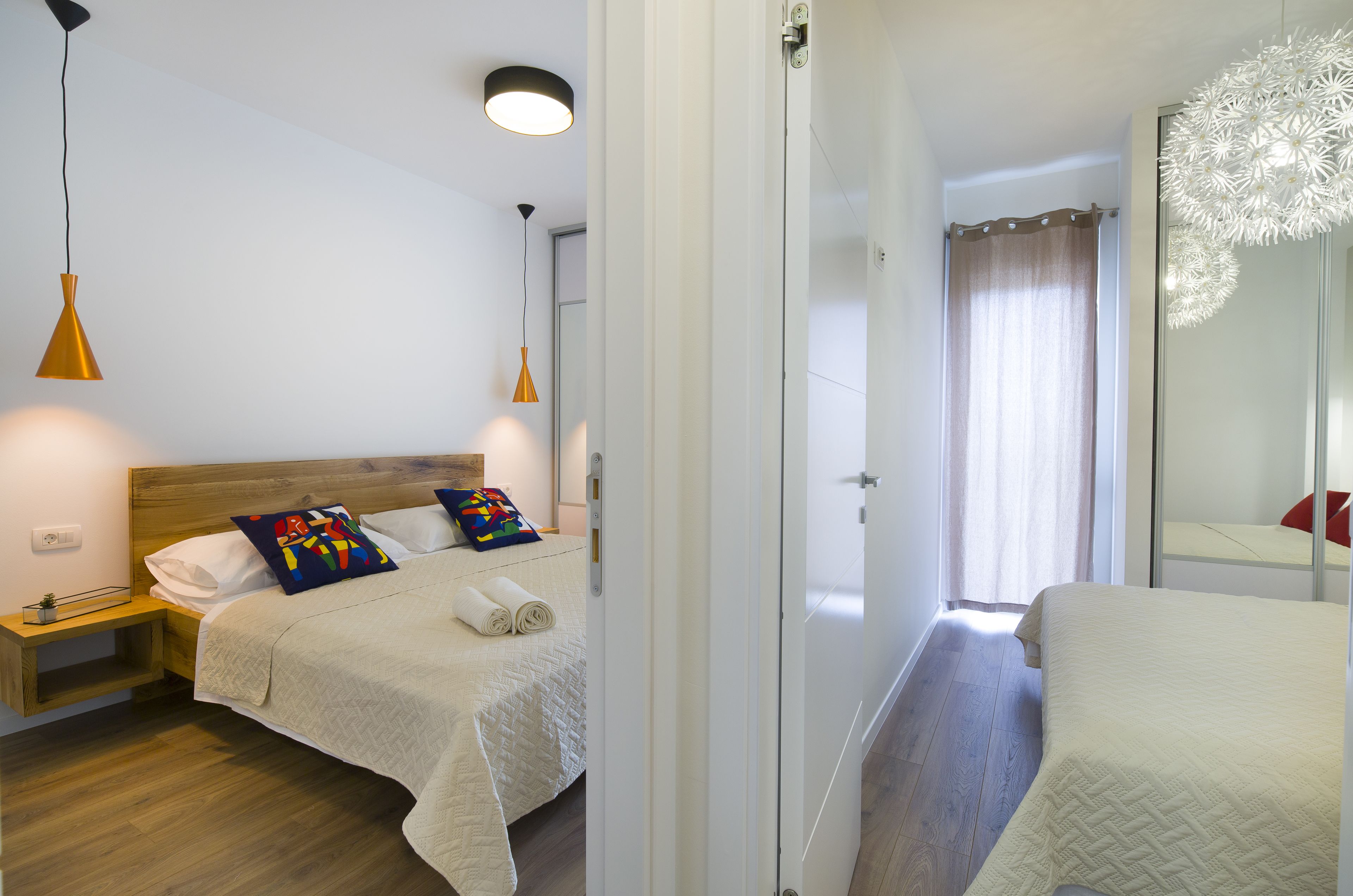 A bedroom with a bed, bedside tables, a nightstand, a mirror, and a hanging light fixture.