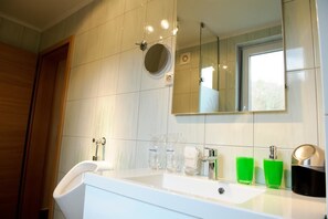 A modern bathroom with a white sink, a mirror, and a window. - Apartments Olimian (Podcetrtek)