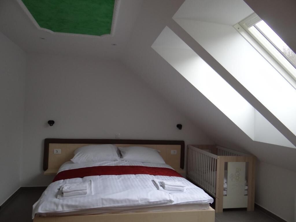 Une pièce avec un plafond en pente, un lit avec une literie blanche rehaussée d’une touche de rouge, un berceau et une fenêtre laissant entrer la lumière naturelle.
