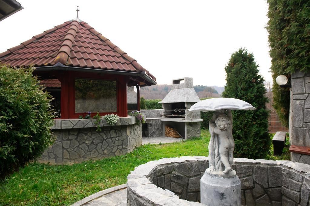 Une terrasse en pierre avec une statue, un espace barbecue et une construction surmontée d’un toit rouge.