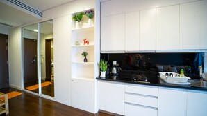 Een moderne keuken met witte kasten, een zwart aanrechtblad en een ingebouwde kookplaat. Er staan planken met decoratieve objecten en een potplant.