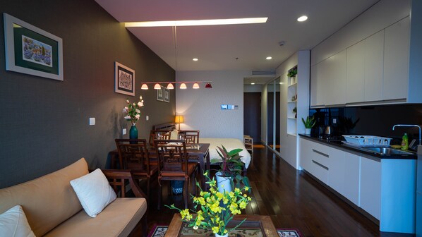 A modern living room with a sofa, dining table, and chairs. There is a kitchen area with cabinets and a sink.