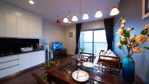 Een moderne keuken met witte kastjes, een zwart aanrecht en een waterdispenser. Er is een zithoek met een houten tafel gedekt voor twee personen, een vaas met bloemen en een televisie op een meubel.
