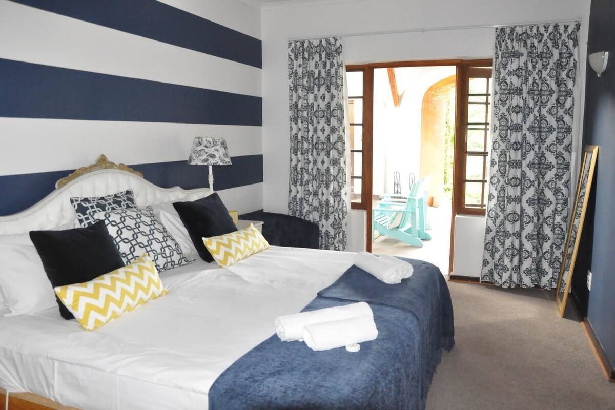 A hotel room with a bed, pillows, a nightstand, and a view of the outside.