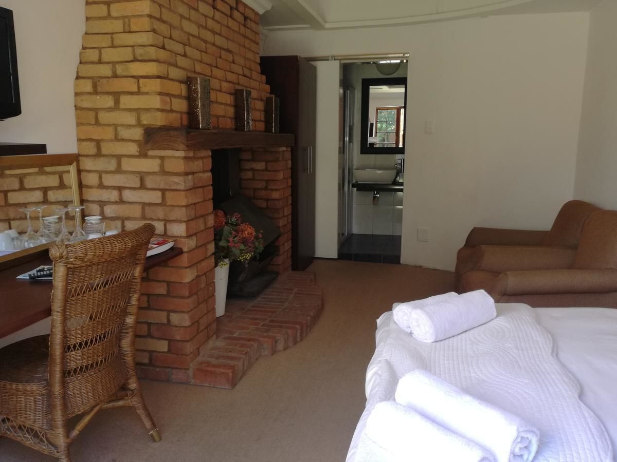 Quarto de hotel com lareira de tijolos, área de jantar com móveis de vime, cama com lençóis brancos e banheiro com espelho e pia.