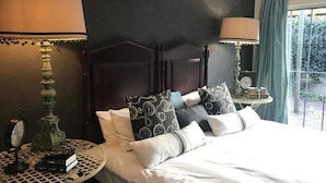 Een net opgemaakt bed met een donker hoofdbord, twee nachtkastjes met lampen, en uitzicht op groen buiten.