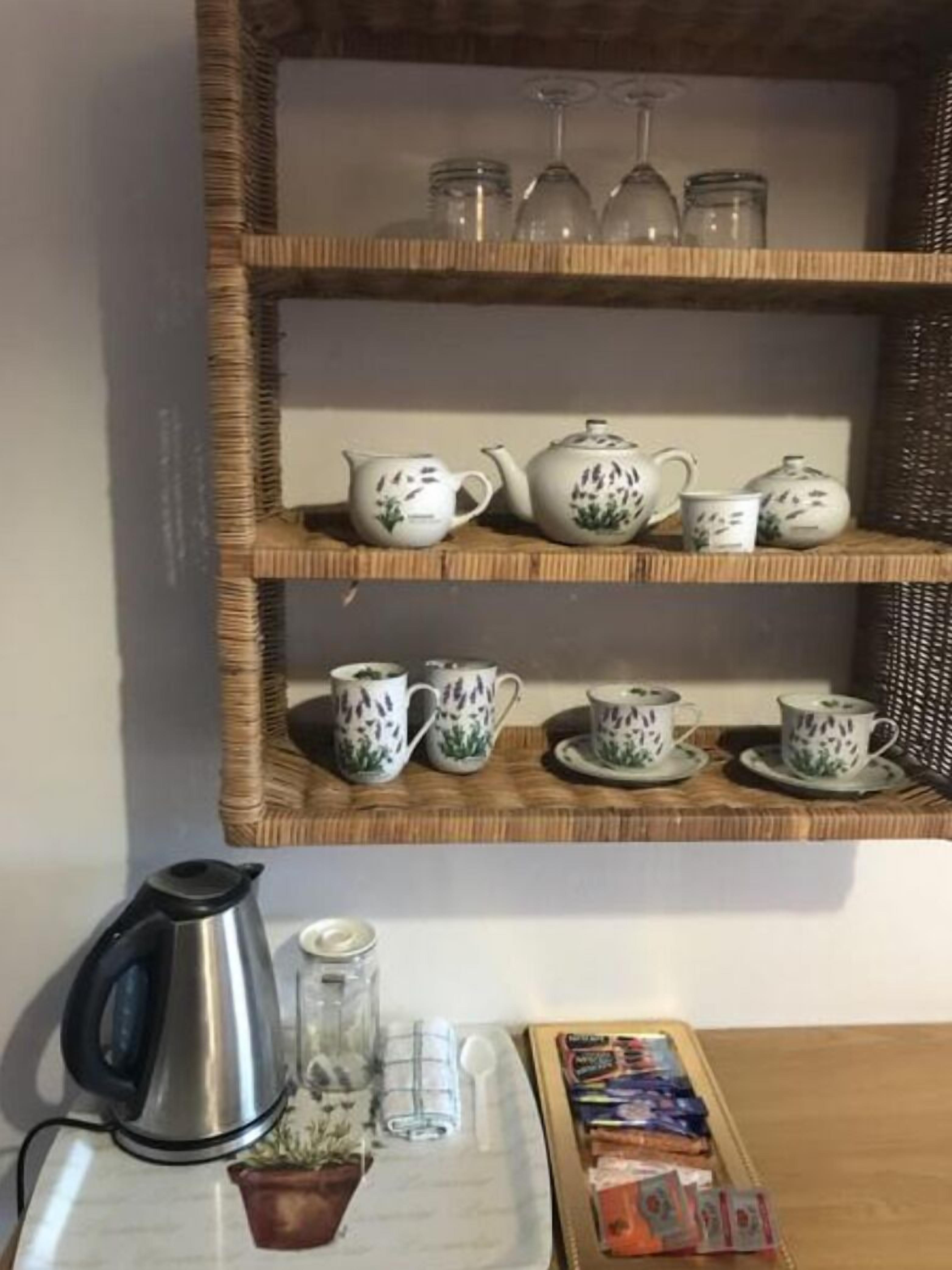 A kitchen area with a wicker shelf holding various tea sets and glassware.