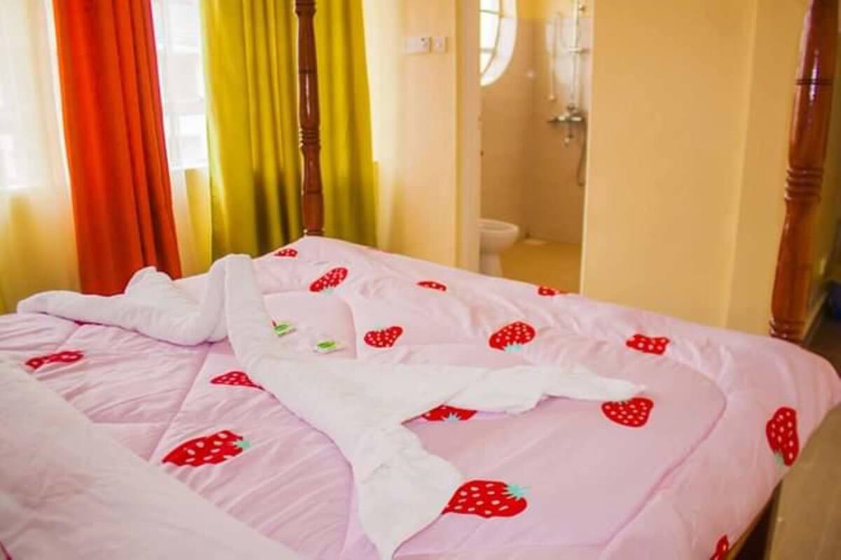 A bed with a pink bedspread featuring strawberry patterns, a wooden headboard, and curtains in red and yellow.