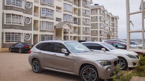 A multi-story residential building with balconies and a parking area with cars. - JKIA Tours and Homes (Syokimau)