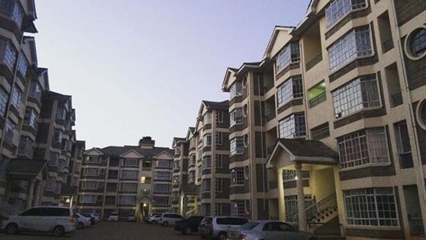 A multi-story residential building with a central courtyard and a parking area. - JKIA Tours and Homes (Syokimau)