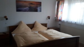 A bedroom with a bed, two bedside tables, a nightstand, a wall-mounted lamp, and a window with curtains. - Gasthaus Kehrwieder (Wunstorf)