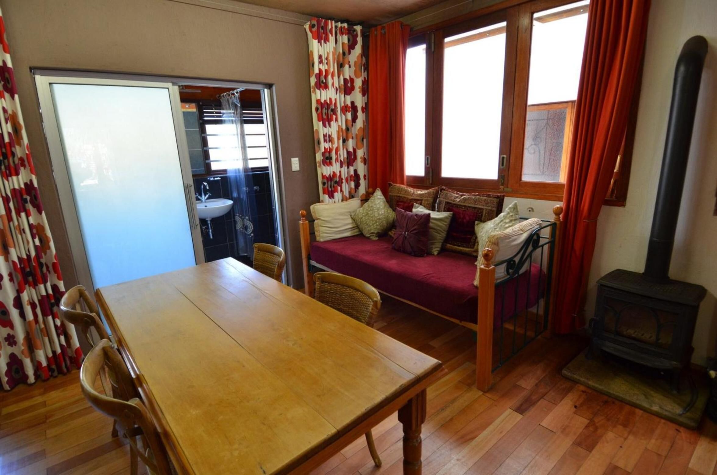 A cozy living room with a wooden table, a sofa with cushions, a fireplace, and a sliding door leading to a bathroom.