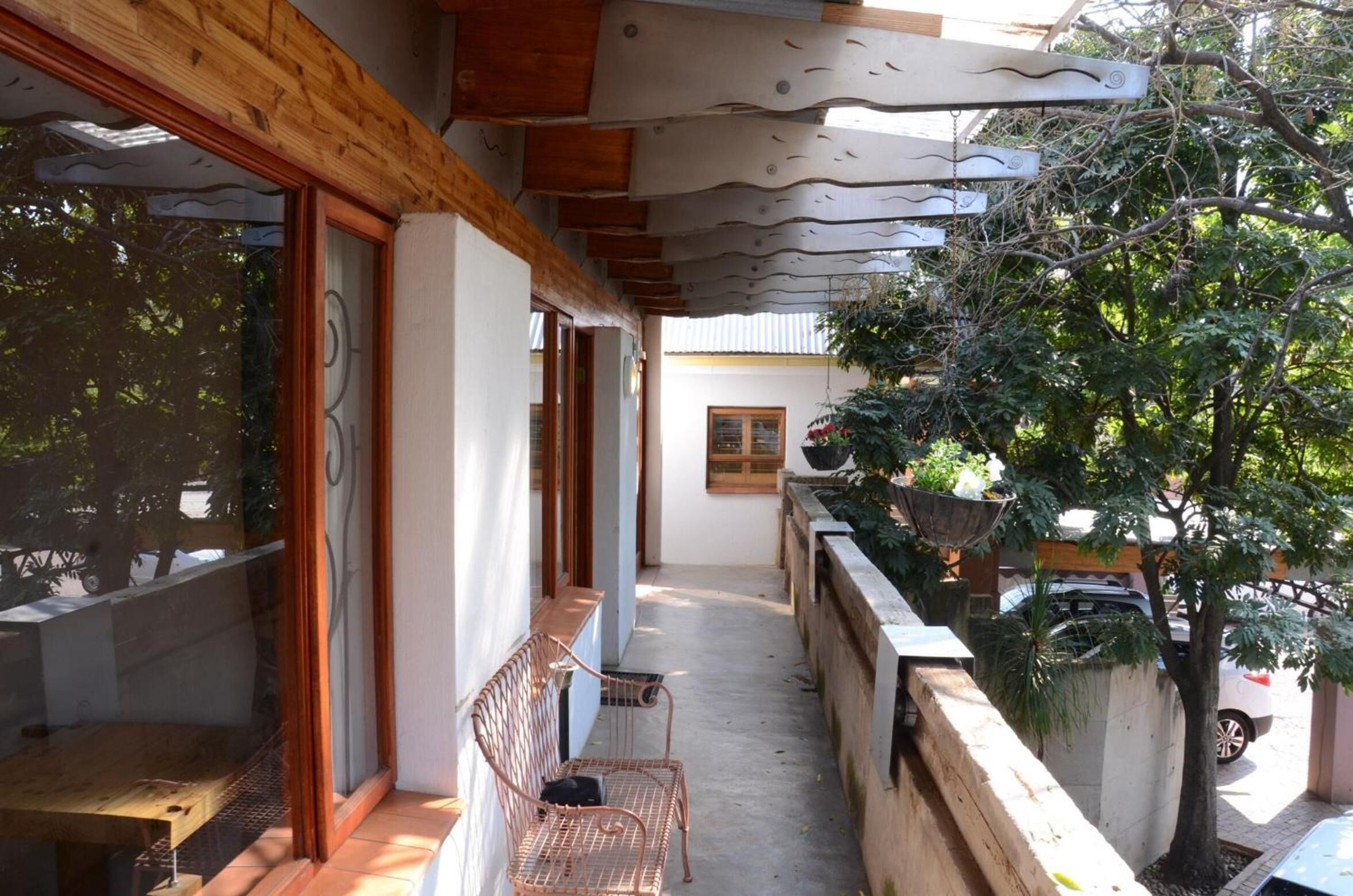 A narrow balcony with a wooden ceiling, a metal bench, and a potted plant.
