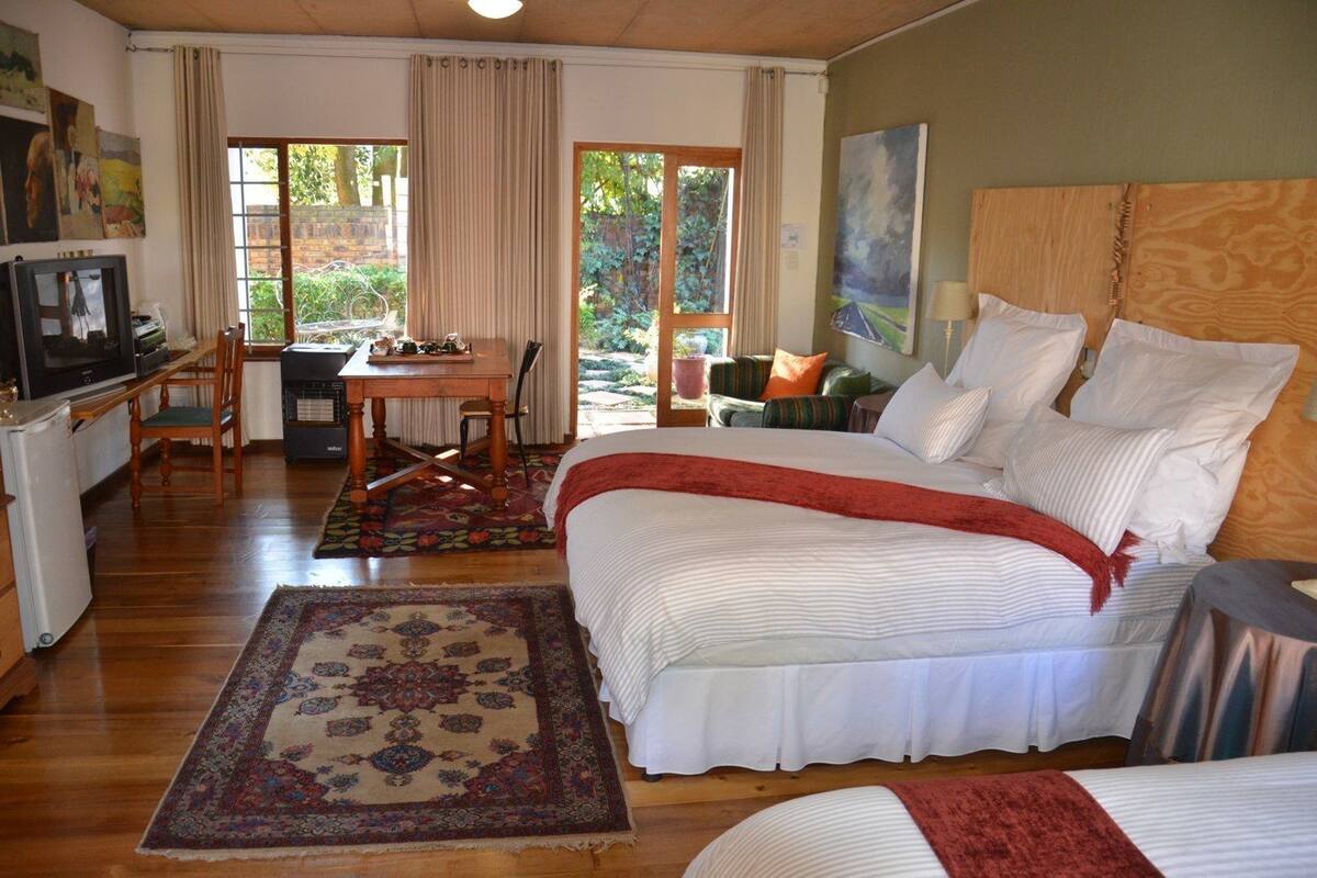 A bedroom with a large bed, a desk with a chair, a television, and a view of the outdoors.