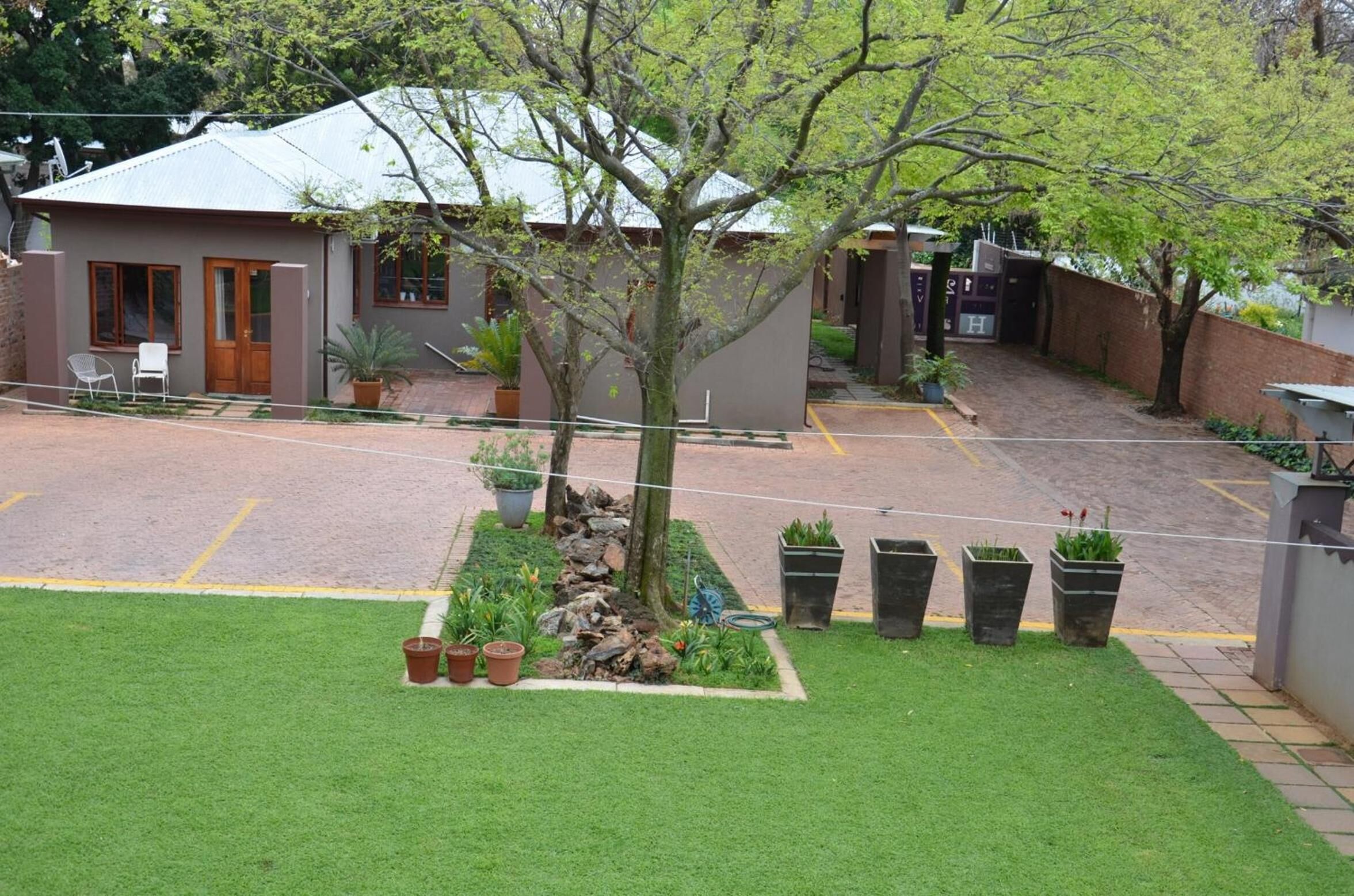 A courtyard with a small building, a tree, and a paved area with potted plants.