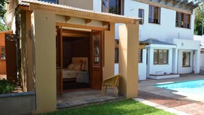 Una pequeña estructura al aire libre con una puerta que da a un dormitorio, una piscina y un edificio blanco al fondo.