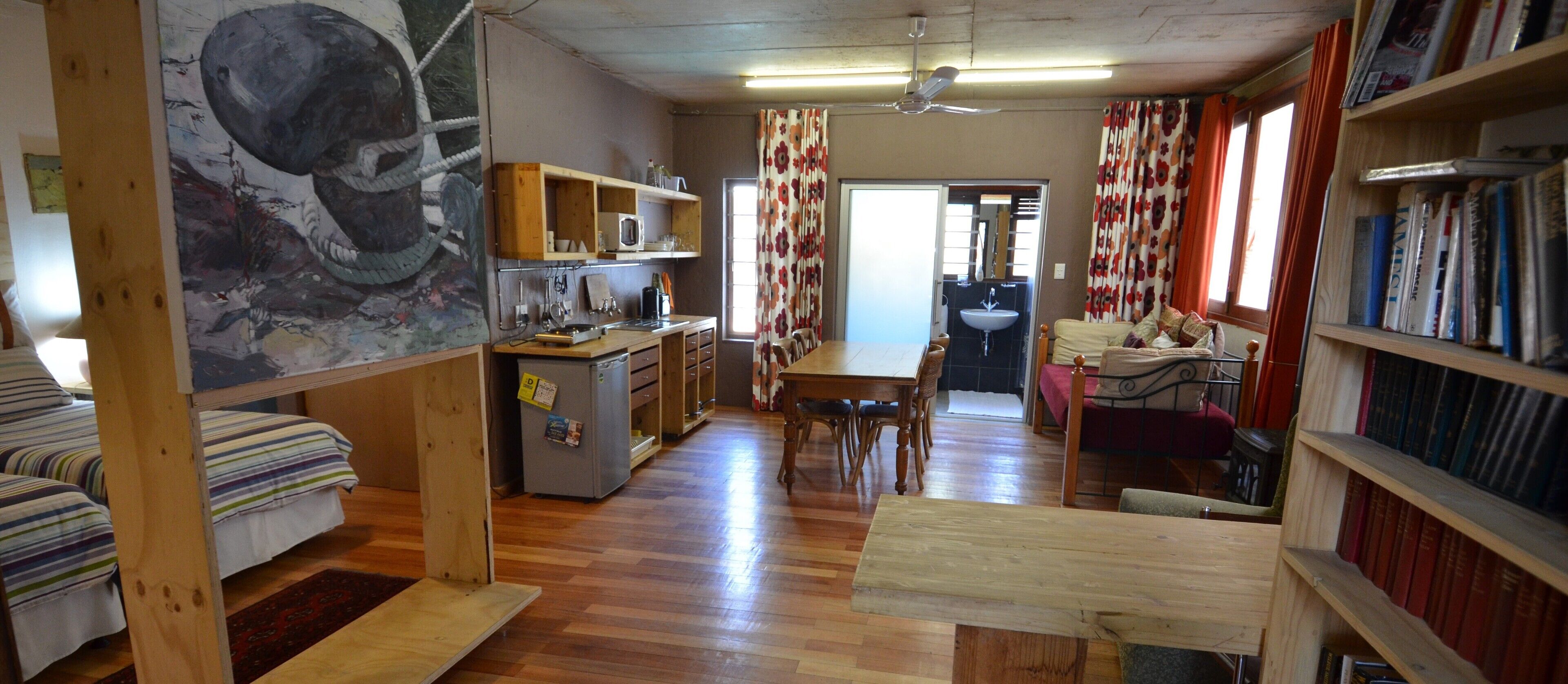 Una habitación acogedora con una cama, un escritorio, una silla, una estantería y una mesa de comedor.