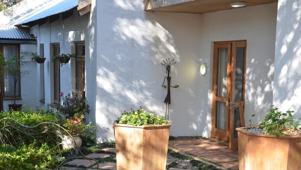 Un patio con un edificio blanco, una puerta de madera y macetas colgantes de flores.