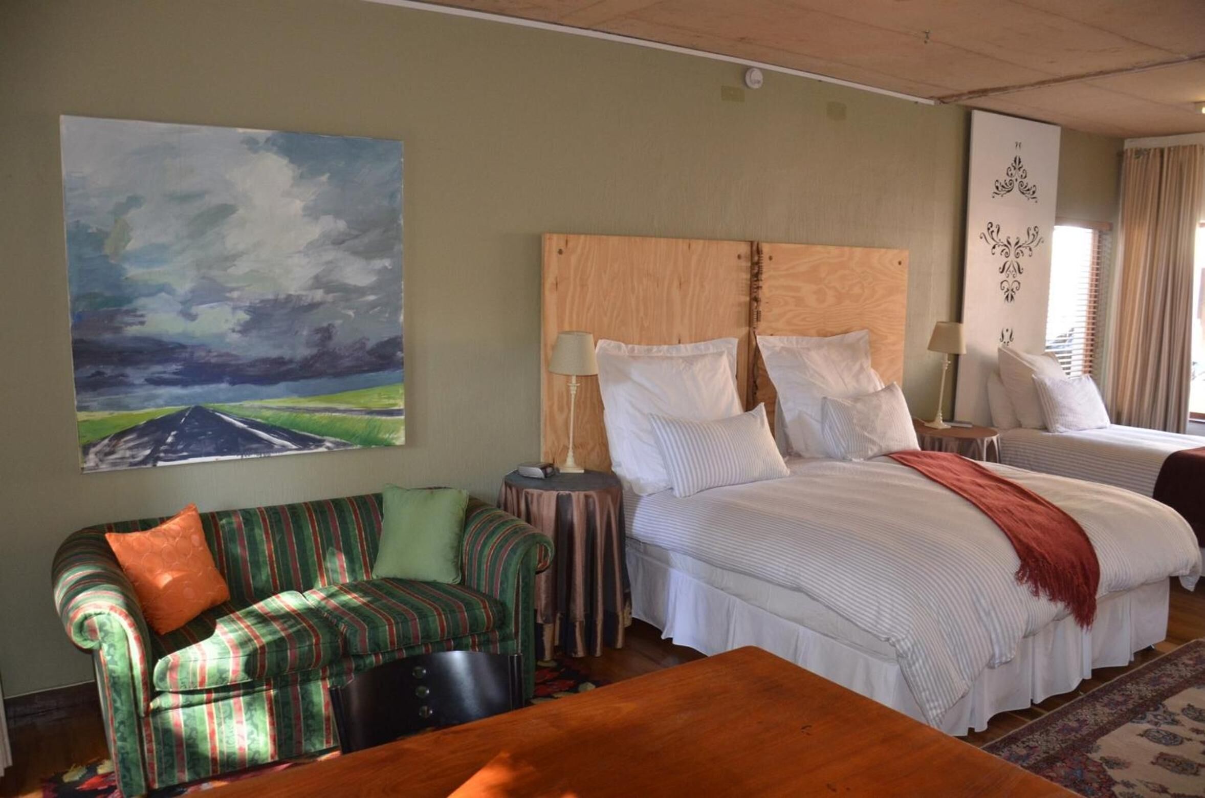 A hotel room with a large bed, a smaller bed, a striped sofa, a wooden table, and a painting of a landscape.