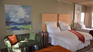 A hotel room with a large bed, a smaller bed, a striped sofa, a wooden table, and a painting of a landscape.