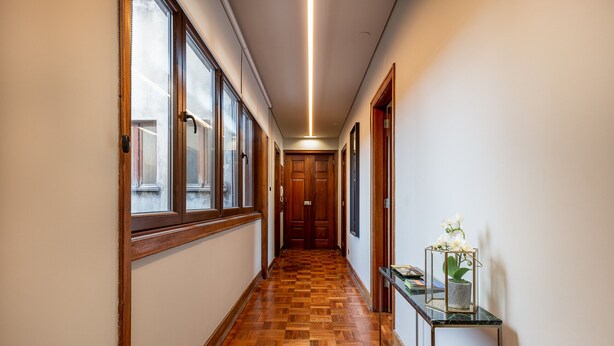 A hallway with wooden flooring, large windows, and a table with a potted plant. - Central 4-Bedroom Apartment in Santa Catarina (Oporto)