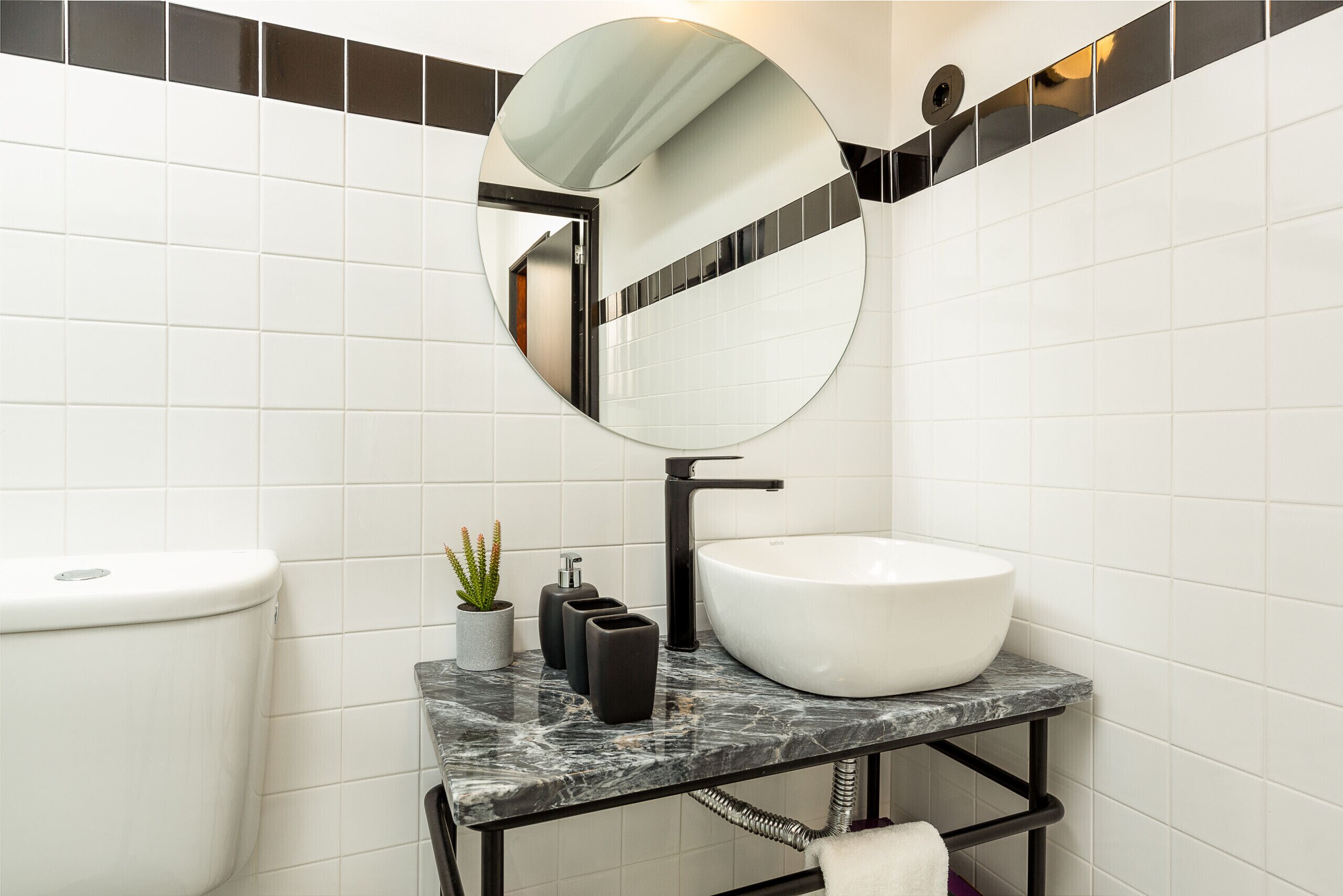 A modern bathroom with a white toilet, a round mirror, a white sink, and a marble countertop.