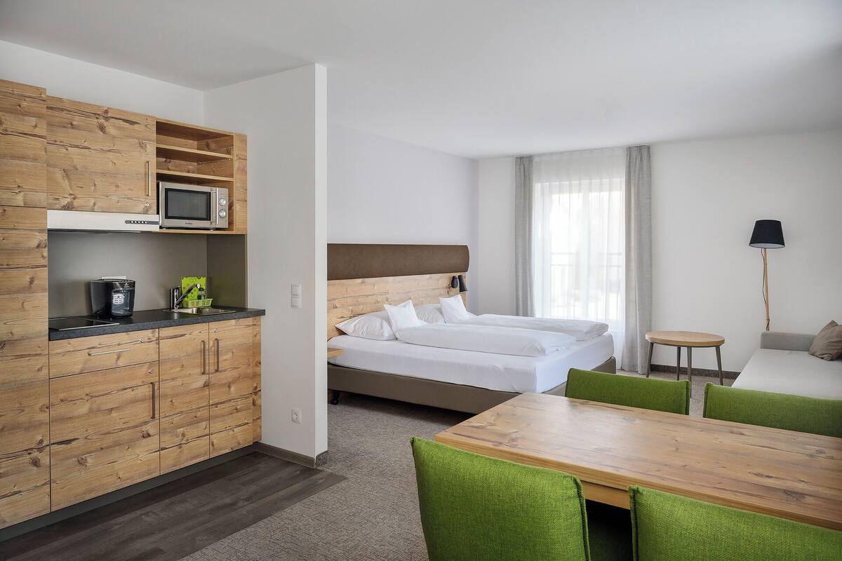 A hotel room with a bed, a wooden dining table, a kitchenette with a microwave, and a small round table.
