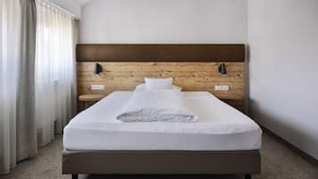 Ein ordentlich bezogenes Bett in einem Hotelzimmer, mit einem hölzernen Kopfteil, einem kleinen Nachttisch und einer Wandlampe.