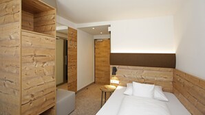 A modern hotel room with a wooden headboard, a bed with white linens, a small round table, and a wooden wardrobe. - ApartHotel Rose Ellwangen (Ellwangen)