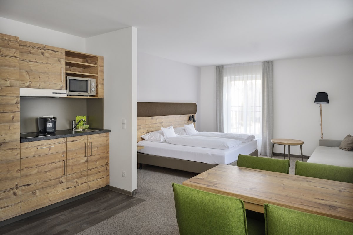 A hotel room with a kitchenette, a bed, a dining area, and a small table.