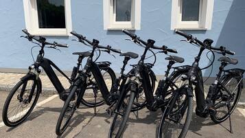 A row of black bicycles parked in front of a blue building with three windows.