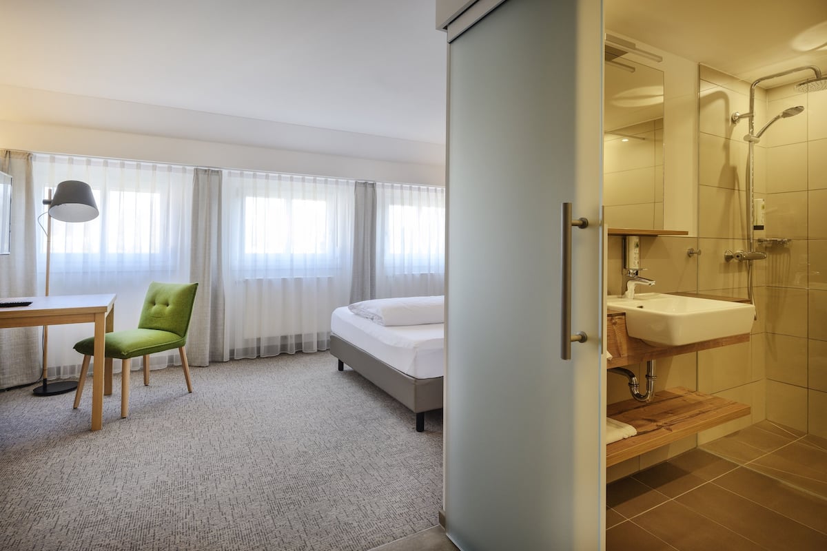 A hotel room with a bed, a desk with a chair, a bathroom with a sink and shower.