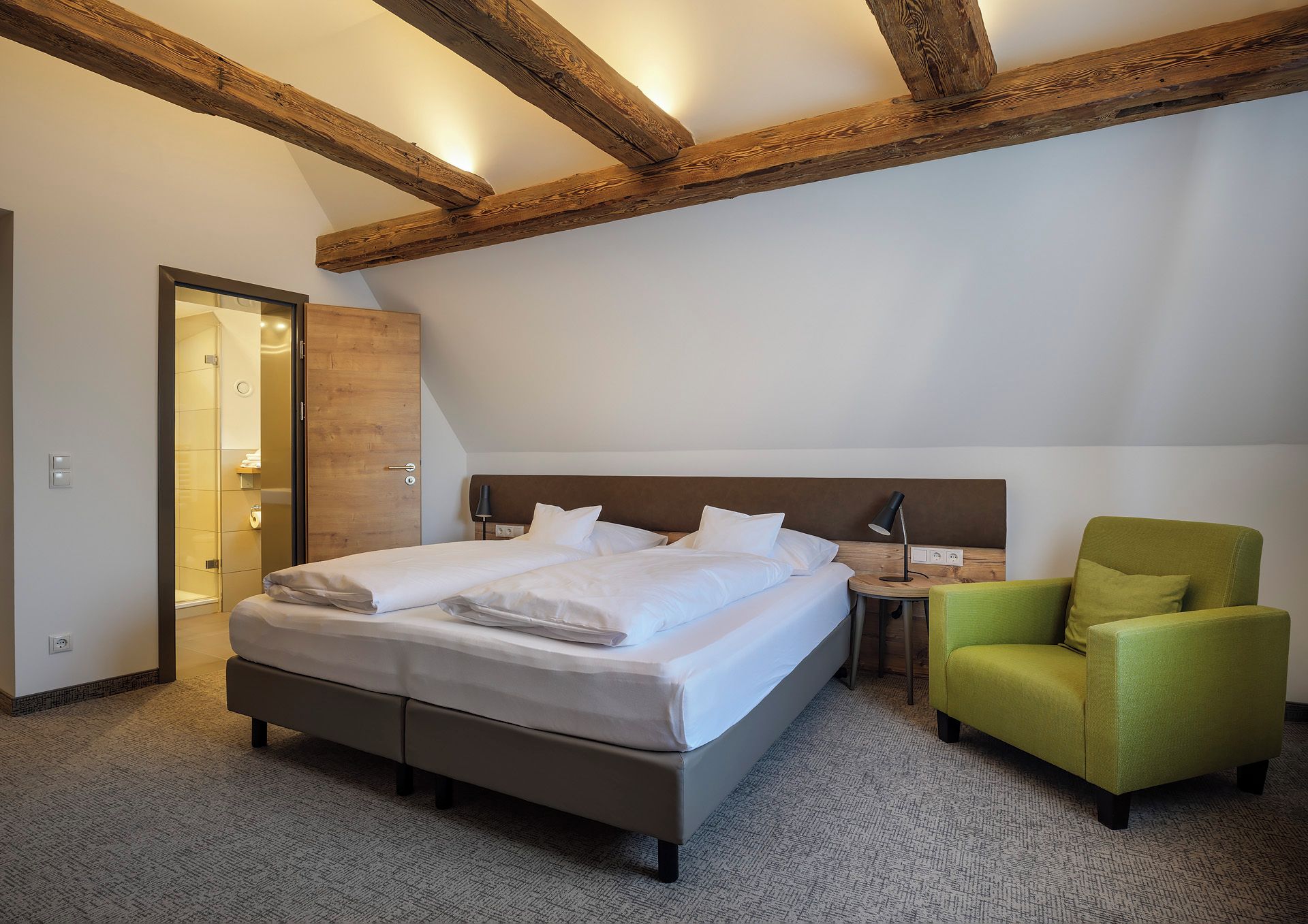 Ein Hotelzimmer mit einem großen Bett, einem grünen Sessel und freiliegenden Holzbalken an der Decke.