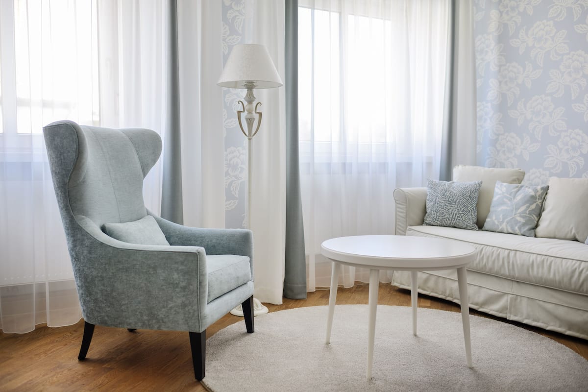 A modern living room with a grey armchair, a white round table, and a white sofa with patterned cushions.
