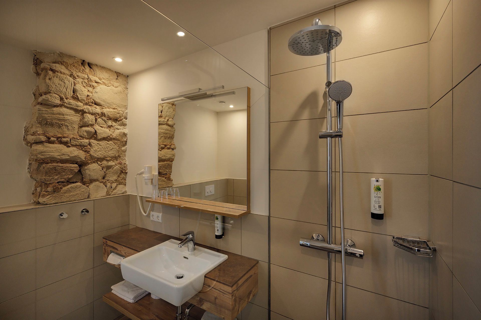 A modern bathroom with a stone accent wall, a sink, a mirror, and a shower with a handheld showerhead.