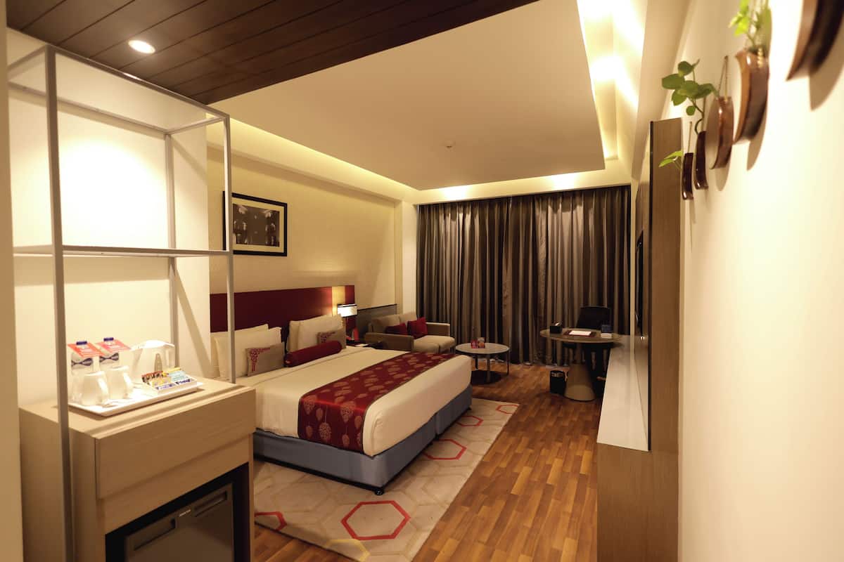 A hotel room with a bed, bedside table, lamp, and a small seating area with a table and chairs.