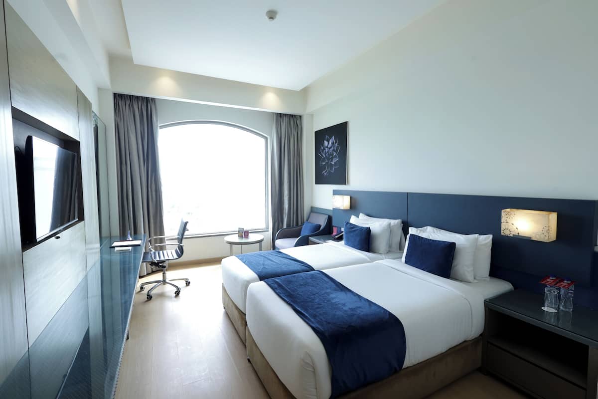 A hotel room with a large bed, a desk, a chair, a TV, and a window with curtains.